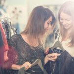 Young friends searching clothes in secondhand clothing shop